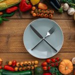 Top view of fresh vegetables creatively arranged around an empty plate on a wooden table.