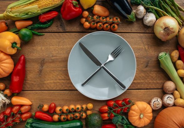 Top view of fresh vegetables creatively arranged around an empty plate on a wooden table.
